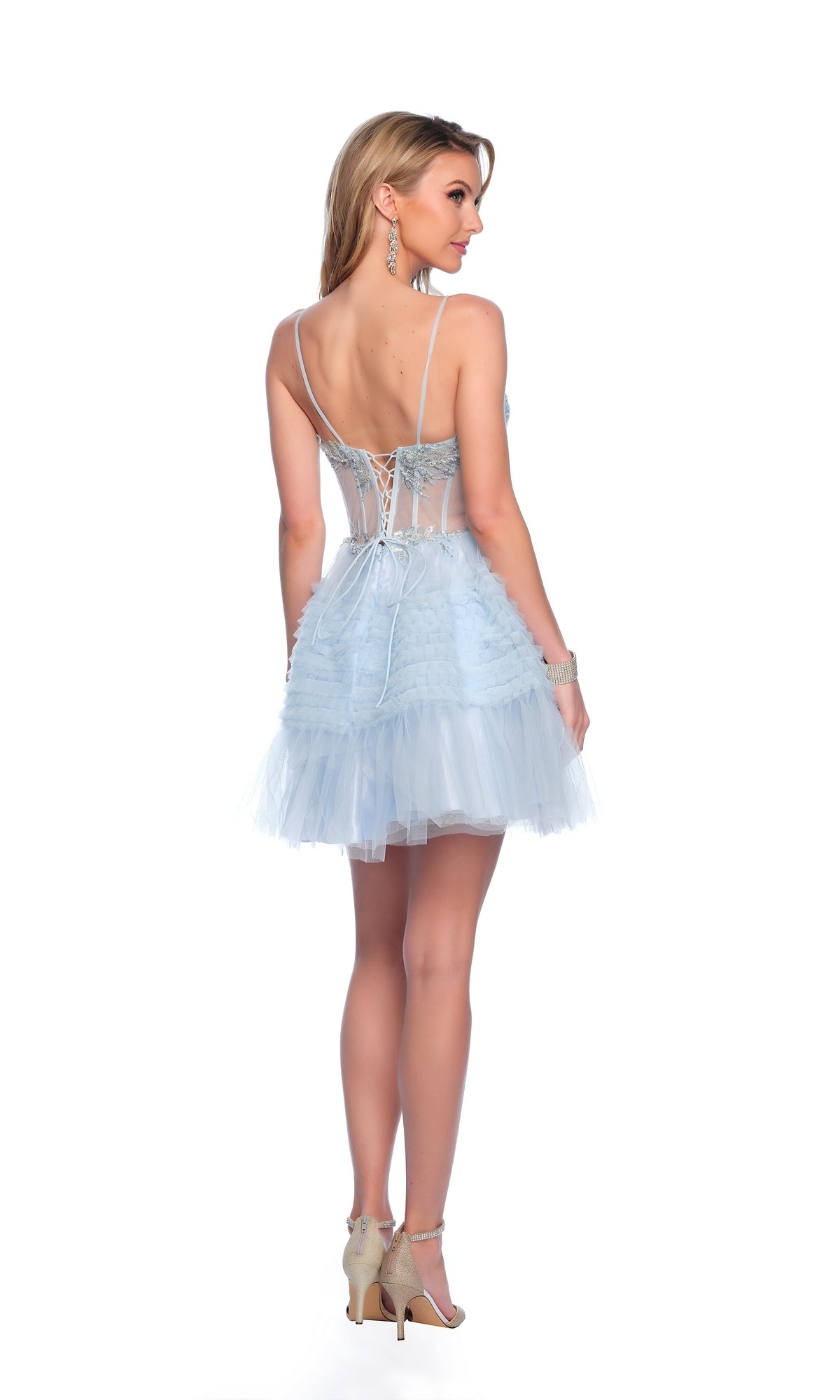 Woman wearing the Dave & Johnny Short Blue Ruffled Hoco Dress 11888, featuring a lace-up corset bodice and tulle skirt, stands in high heels with her back to the camera against a white background.